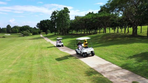 Aerial view group of Asian people businessman and senior CEO sitting on driving golf cart at golf course in sunny day. Healthy male friends golfer golfing together at country club in summer vacation