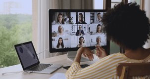 Group of diverse businesspeople involved in discussion, solve business remotely use videocall, pc screen view over African businesswoman shoulder sit at desk taking notes negotiates through video call