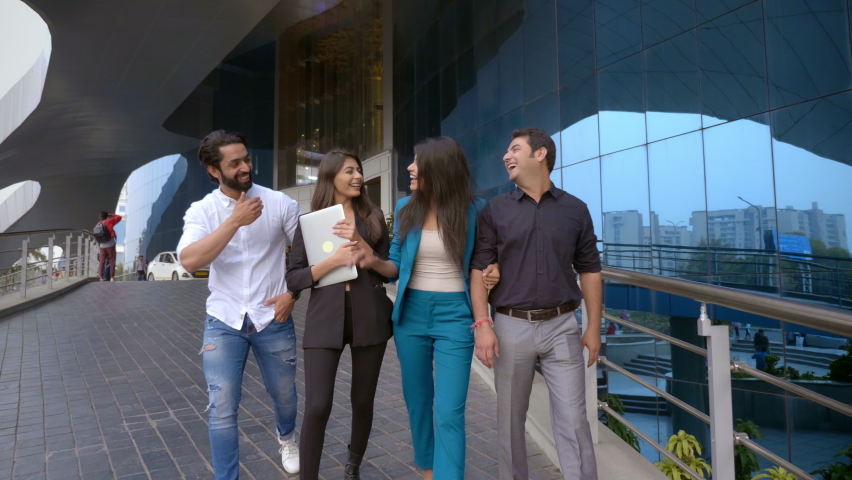 A happy Indian attractive group of male and female office employees walking next to a modern commercial complex. A mixed team of corporate or start up business partners are smiling and interacting Royalty-Free Stock Footage #1085934527