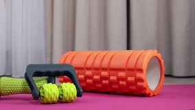 On pink background, colored exercise equipment for yoga and myofascial massage of legs and feet at home. A large orange and a small green roll, prickly and green balls for acupuncture points on body