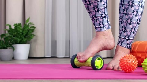 A girl in sportswear Veri Perry on a pink yoga mat makes myofascial foot massage at home to improve blood flow with a special green foot roller, presses on acupuncture points. Close-up of the leg, one