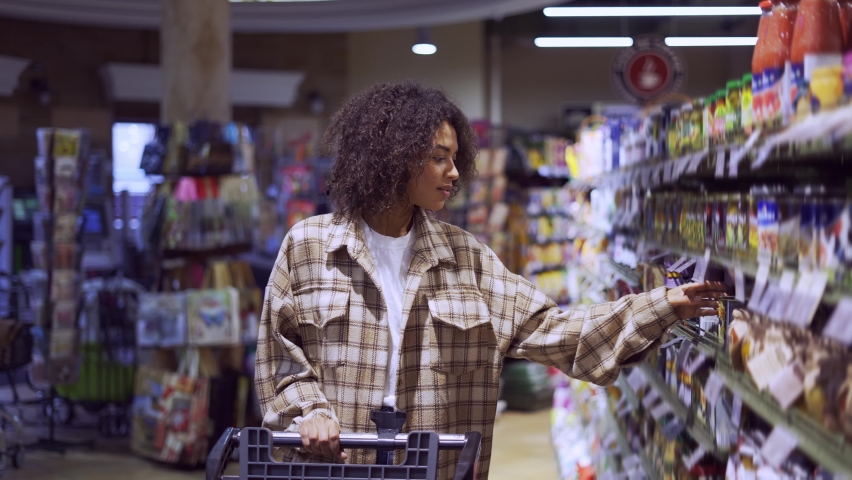 Lovely woman walking through aisle in supermarket with shopping cart looking at shelves Royalty-Free Stock Footage #1085937779