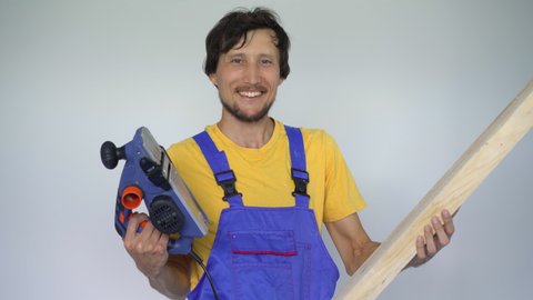 A man professional tile installer a wooden plank and an electric planer in his hands. He looks at the camera smiling