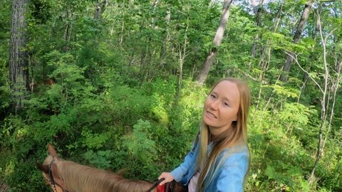 Woman is riding a horse in a forest. She shoots a selfie video