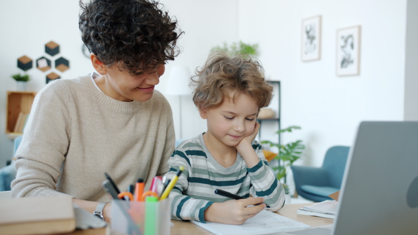 Kid learning with mother at home writing and looking at laptop screen in apartment. Modern education and intelligent family activity concept. Royalty-Free Stock Footage #1085939681