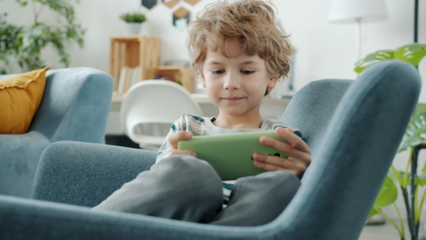 Child is playing mobile game with smartphone touching screen and smiling indoors at home. Modern technology and happy childhood concept. | Shutterstock HD Video #1085939696