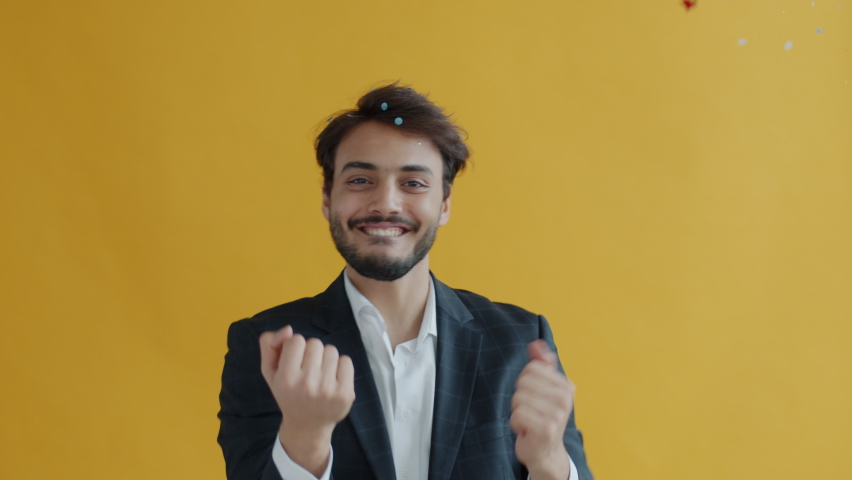 Portrait of Middle Eastern dancer moving while confetti falling down in air during holiday celebration. Man in elegant suit dancing on yellow background. Royalty-Free Stock Footage #1085939741