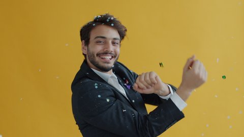 Portrait of Middle Eastern dancer moving while confetti falling down in air during holiday celebration. Man in elegant suit dancing on yellow background.