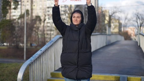 Portrait of serious young woman standing on urban city bridge with anti-vax placard. Confident Caucasian protestor against mandatory coronavirus vaccination rioting outdoors on autumn spring day