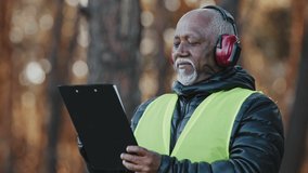 Close-up african american male professional foreman forestry engineer standing outdoors wearing protective headphones assessing situation making tree felling plan writing data reforestation projectt - Powered by Shutterstock - Get 15% off with code: PIKWIZARD15