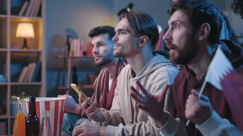 Excited people looking attentively at the device screen and feeling overjoyed while gesturing with fists. Fans feeling blessed of sports betting during football game at home concept | Shutterstock HD Video #1085958215