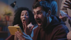 Agitated guy rejoicing while watching over sports betting at the smartphone screen. Focus on the man with device smiling and looking at the friends while sitting on sofa. Sport fans concept - Powered by Shutterstock - Get 15% off with code: PIKWIZARD15