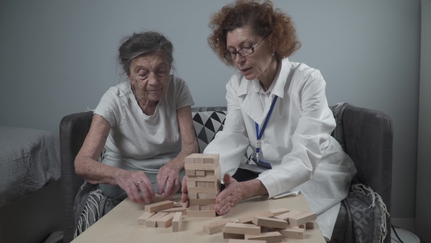 Mature doctor conducting session, therapy for senior patient in nursing home, training fine motor skills for dementia, alzheimer disease and recovery institute by folding wooden blocks, playing jenga Royalty-Free Stock Footage #1085958626