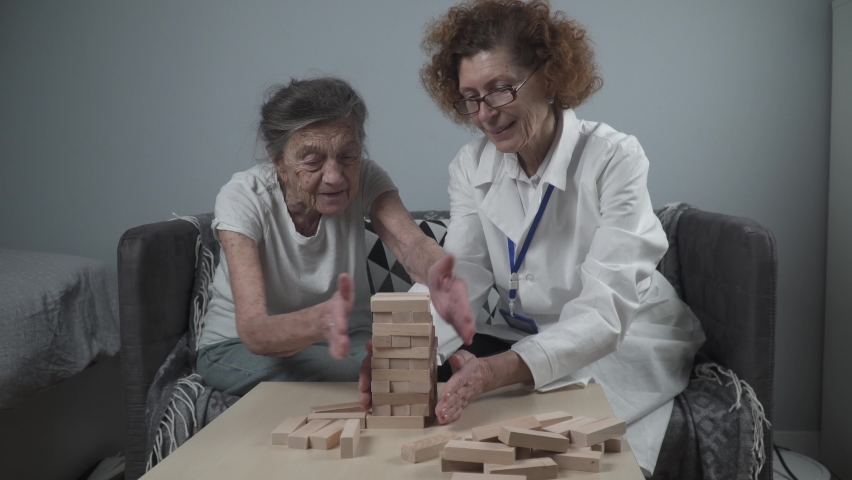 Mature doctor conducting session, therapy for senior patient in nursing home, training fine motor skills for dementia, alzheimer disease and recovery institute by folding wooden blocks, playing jenga | Shutterstock HD Video #1085958626