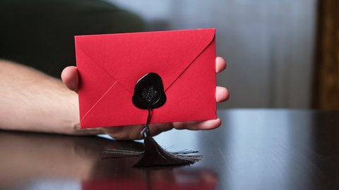 A red envelope sealed with sealing wax in a man's hand. Correspondence, love letter concept.