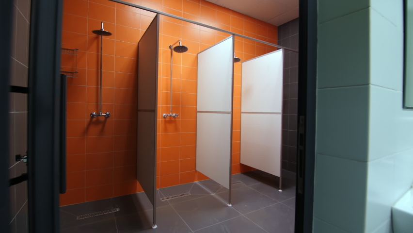 Empty shower cabins with new equipment separated by enclosure partitions at bright orange tiled wall in contemporary sports complex Royalty-Free Stock Footage #1085960813