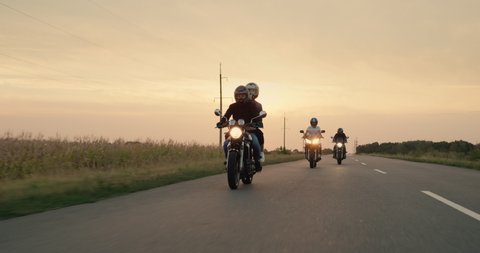 Three bikers drive on the highway at sunset
