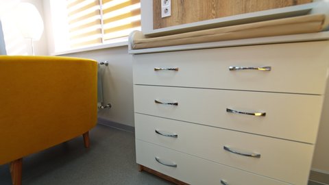 Well-furnished room in maternity hospital. White chest of drawers with changing table and other furniture in the ward for mother and child after birth.