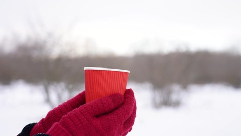 Close up view slow motion 4k stock video footage of female hands in red gloves holding paper cup standing outdoor in snowy winter landscape