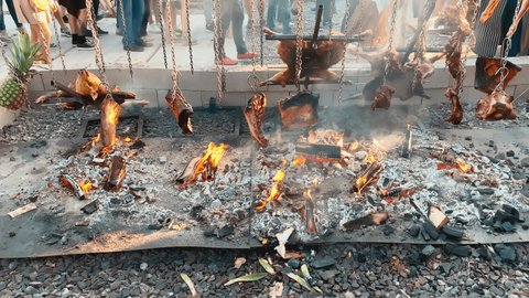 Large chunks of pork, beef and pineapple meat are cooked on a huge grill, burning logs on a sheet of iron as coals, the pig's head is baked on an open fire.
