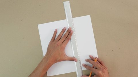 Trace a 3x3 grid on white cardboard. Craft paper background. Ruler and pencil are used. Brown hands. School activity. 