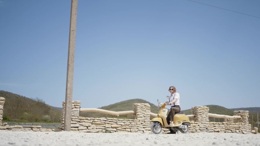 Summer landscape with a man. Action. A handsome man with long hair on a small green motorcycle on a beautiful landscape with blue sky and mountains.