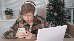A teenage boy with headphones is holding a mobile phone in his hands and studying information in it. Distance learning, an online lesson with a tutor teacher using a video conferencing application.