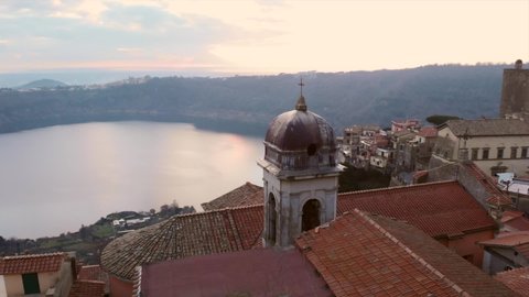 Calm and quite aerial view of the italian village Nemi between the green trees during a beautiful sunset with in the background Nemi lake. forward drone shot through the church top