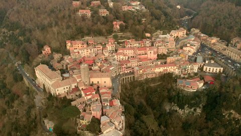 Calm and quite aerial view of the italian village Nemi between the green trees during a beautiful sunset with in the background an high mountain. forward aerial shot