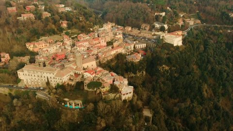 Calm and quite aerial view of the italian village Nemi between the green trees during a beautiful sunset with in the background an high mountain. Backwards drone pan shot