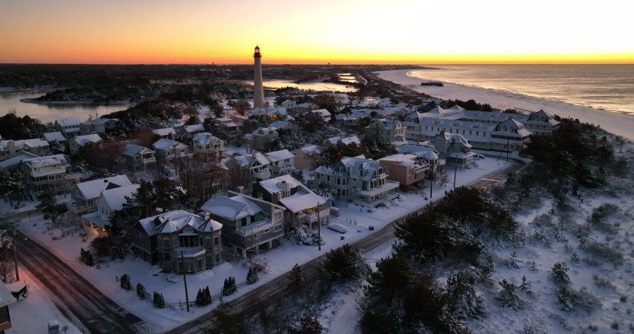Seaside resort town and lighthouse. Cape May Point New Jersey covered in winter snow at sunset. Gorgeous aerial.