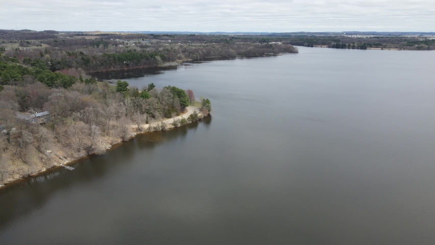 Aerial view over Mississippi River in autumn. Bare trees along the coastline with several boat docks. Mountains and cloudy blue sky in the distance. 