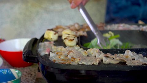Hand of woman is using chopsticks to chop pork in the electric sukiyaki pot.