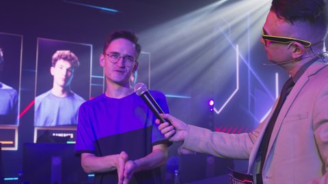 Host taking interview young gamer esportsman before battle while standing under neon illumination at start of gaming championship