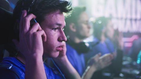 Anxious teen esportsman gamer touching face and putting on headphones then bumping fists with teammate at start of professional gaming competition