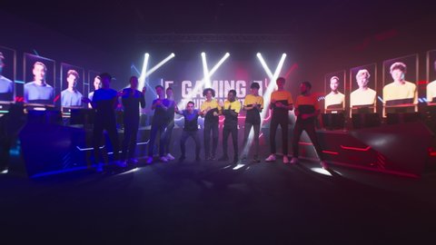 Group of teammates esport gamers walking and clapping hands then standing in front of monitor with gaming tournament banner at start of championship.