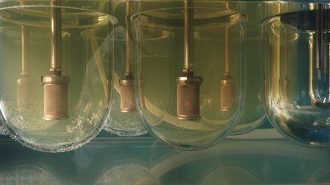 Pills Stirred In The Cylindrical Basket Put In Light Yellow Liquid. Dissolution Apparatus For Analyzing Medicine Samples. Close Up. Laboratory Testing. Measuring Of Medicine Composition Quality.