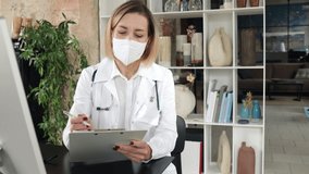 Middle aged female in white medical uniform standing speaking looking at camera make video chat conference call or recording healthcare webinar training talk to distant patient.