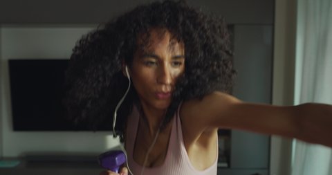 Cinematic shot of young sporty brazilian woman with athletic body wearing bra and leggings is practicing high intensity cardio exercises with dumbbells at home during covid-19 pandemic lockdown.
