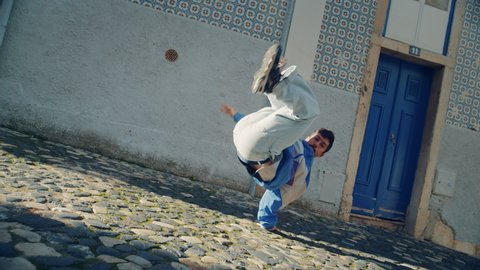 Slow Motion Shot of a Young Adult Latin Man in Stylish Clothes Actively Breakdancing on the Street of an Old Town in a City. Scene Shot in an Urban Environment on an Quiet Small Town Street.