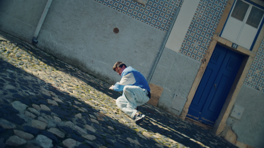 Active and Cheerful Young Adult Latin Man in Stylish Clothes Actively Breakdancing on the Street of an Old Town in a City. Scene Shot in an Urban Environment on an Quiet Small Town Street. Royalty-Free Stock Footage #1085991650