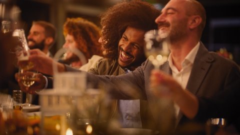 Big Dinner Party with a Small Crowd of Multiethnic Diverse Friends Celebrating at a Restaurant. Beautiful Happy Hosts Propose a Toast and Raise Wine Glasses while Sitting at a Table in the Evening. Video stock