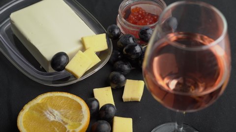 The girl takes a glass of rose wine on the background of snacks. Aesthetics of wine with cheese. Alcohol, romance, evening. Cheese, butter, red caviar, grapes, baguette, orange. View from above.