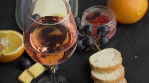 A glass of ros wine swirls with appetizers. Aesthetics of wine with cheese. Alcohol, romance, evening. Cheese, butter, red caviar, grapes, baguette, orange. View from above.