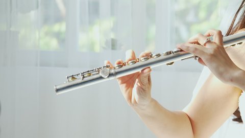 A charming female flutist performs on her instrument. A young and elegant Asian woman plays the flute
