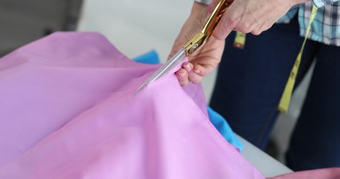 Fashion designer cutting clothes in atelier, working in textile workshop closeup