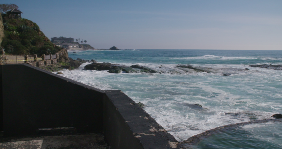 Pacific waves crash into shore as the camera reveals Victoria Beach Pirate Tower in Laguna Beach, California.