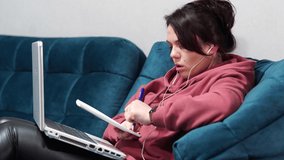 Girl sitting on sofa with headphones and laptop. Remote work at home on the couch.