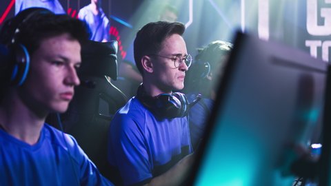 Esportsman gamer in glasses speaking and bumping fists with teammates as inspirational gesture then putting on headset at start of professional gaming championship