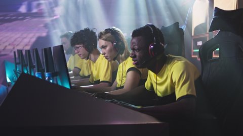 Angry esportsman gamer woman breaking keyboard and screaming then covering face with hands while sitting amidst disappointed teammates after loss in gaming tournament